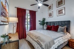 Dallas apartment for rent - A bedroom with a bed, a ceiling fan, and a window with red curtains.