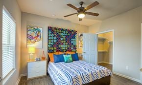 Round Rock apartment for rent - A bedroom with a bed, a ceiling fan, and a wall hanging.
