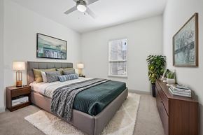 Mckinney apartment for rent - A bedroom with a bed, nightstand, and a plant.