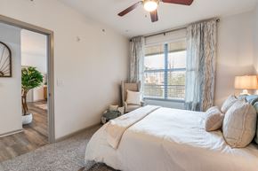 Lewisville apartment for rent - A bedroom with a large bed, a ceiling fan, and a window with blinds.