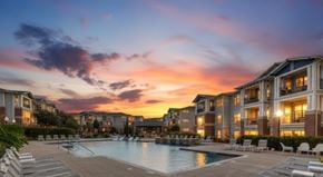 Lewisville apartment for rent - A sunset view of a pool area in front of apartment buildings.