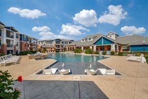 Lewisville apartment for rent - A large swimming pool surrounded by lounge chairs and buildings in the background.