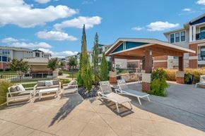 Lewisville apartment for rent - A patio with a couch, chairs, and a tree in front of a building.