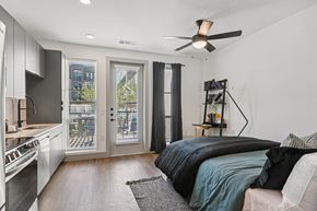 Lewisville apartment for rent - A modern bedroom with a large bed and a kitchen area in the background.