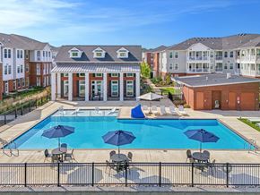 Spring Hill apartment for rent - A swimming pool surrounded by a black fence with blue umbrellas and chairs.