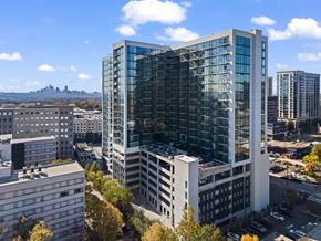 Atlanta apartment for rent - A modern glass building stands tall in a cityscape with other buildings and a distant castle.