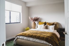 Miami apartment for rent - A bedroom with a bed covered in a mustard yellow comforter and a vase of flowers on the bedside table.