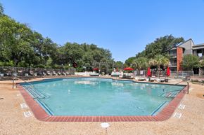 Austin apartment for rent - A large outdoor swimming pool surrounded by trees and a fence.