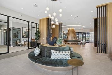 Nashville apartment for rent - A modern living room with a green velvet sofa and a wooden sculpture on a pedestal.