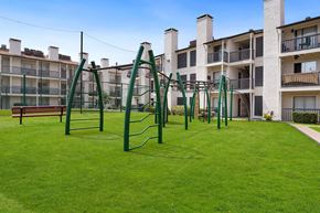 Dallas apartment for rent - a playground with a monkey bars swing set in front of an apartment building
