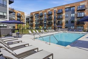 Skokie townhouse for rent - A pool surrounded by lounge chairs and umbrellas in front of apartment buildings.