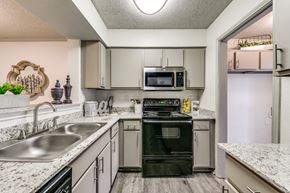 Dallas apartment for rent - a kitchen with white cabinets and black appliances and granite counter tops