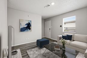 Stephenville apartment for rent - A living room with a blue ottoman, a white couch, and a painting on the wall.