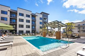 Phoenix apartment for rent - A swimming pool surrounded by lounge chairs and umbrellas in front of a modern apartment building.