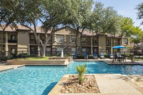 Irving apartment for rent - A swimming pool surrounded by trees and a building in the background.