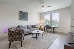 Dallas apartment for rent - A living room with a grey sofa, a patterned chair, a small table, and a ceiling fan.