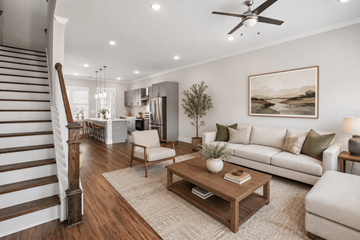 Gallatin townhouse for rent - A living room with a staircase on the left side and a couch with a plant on it.