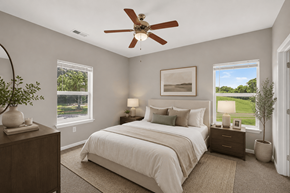 Antioch apartment for rent - A bedroom with a large bed, a ceiling fan, and a view of a green landscape through the windows.