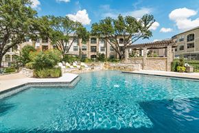 San Antonio apartment for rent - A swimming pool surrounded by a stone wall and trees.
