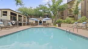 Round Rock apartment for rent - a swimming pool with lounge chairs and umbrellas in front of a building
