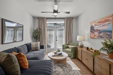 Austin apartment for rent - A living room with a grey sofa, a coffee table, a ceiling fan, and a painting on the wall.