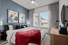 The Colony apartment for rent - A bedroom with a bed covered in a red blanket and a ceiling fan above it.