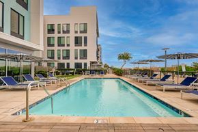 Tempe apartment for rent - A large swimming pool with lounge chairs and umbrellas in front of a modern building.