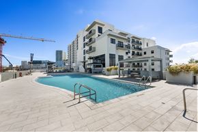 Miami apartment for rent - A large swimming pool is surrounded by a tiled patio and a building with balconies.