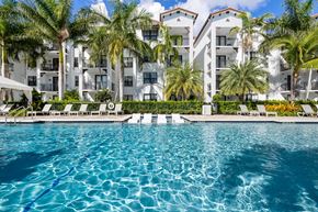 Naples apartment for rent - A swimming pool in front of a white building with palm trees.