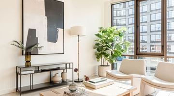 Atlanta apartment for rent - A living room with a large painting on the wall, a white sofa, a coffee table with books and vases, and a potted plant.