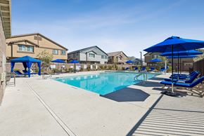 North Las Vegas apartment for rent - A swimming pool surrounded by blue umbrellas and lounge chairs.