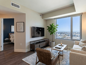 Oakland apartment for rent - A living room with a brown chair, a white coffee table, and a large window overlooking the city.