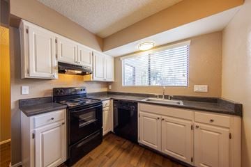 Tucson apartment for rent - a kitchen with white cabinets and black appliances and a window