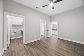 Dallas apartment for rent - A spacious room with a ceiling fan and light, hardwood floors, and a view into another room through an open door.
