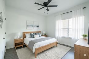 New Braunfels apartment for rent - A bedroom with a large bed, a ceiling fan, and a window with white curtains.