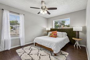 Austin apartment for rent - A bedroom with a bed, a ceiling fan, and a window with white curtains.