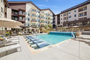 Anna apartment for rent - A large swimming pool surrounded by lounge chairs and umbrellas in front of apartment buildings.