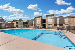 Lubbock apartment for rent - A swimming pool in front of a building with a fence around it.
