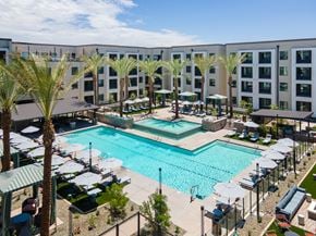 Phoenix apartment for rent - A large swimming pool surrounded by palm trees and lounge chairs.