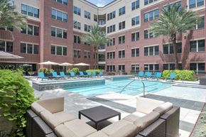 Houston apartment for rent - A large pool surrounded by chairs and umbrellas in front of a brick building.