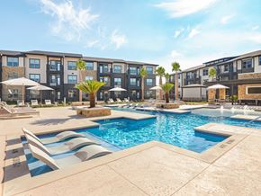 Cibolo apartment for rent - A swimming pool surrounded by lounge chairs and umbrellas in front of a multi-story apartment building.
