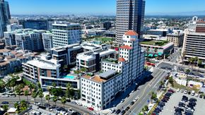 Long Beach apartment for rent - A cityscape with a mix of modern and older buildings, a clear sky, and a busy intersection with cars.