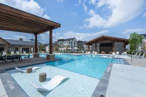 Katy apartment for rent - A large outdoor swimming pool with a wooden roof and lounge chairs.