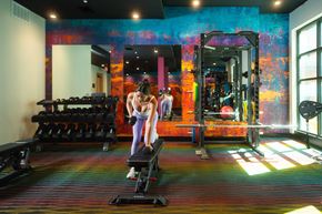 Austin apartment for rent - A woman is exercising in a gym with a mirror and a row of dumbbells.
