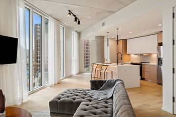 San Antonio apartment for rent - A modern living room with a grey tufted sofa and a kitchen area in the background.