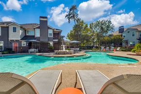 Conroe apartment for rent - A swimming pool surrounded by lounge chairs and a row of houses in the background.