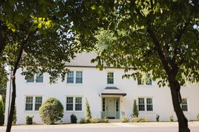 Nashville apartment for rent - A white house with a grey roof and a green door is surrounded by trees.