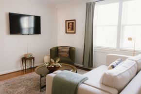 Nashville apartment for rent - A living room with a white couch, a green chair, and a flat screen TV mounted on the wall.