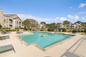 Shreveport apartment for rent - A large swimming pool surrounded by a concrete patio and lounge chairs.