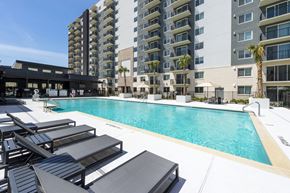 Houston apartment for rent - a swimming pool with lounge chairs in front of a luxury high rise apartment building